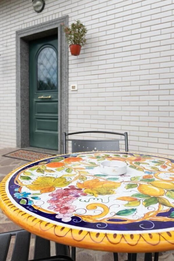 A round table with a colorful floral tablecloth, a green door, and a potted plant on the wall. - castelbarco house (Roma)
