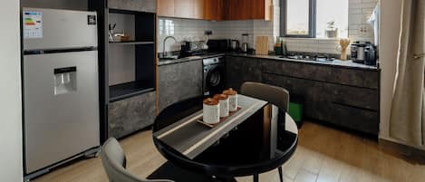 A modern kitchen with a dining table, chairs, a refrigerator, a washing machine, and a window with a view.
