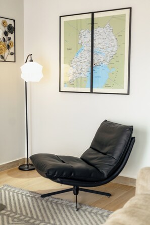 Et værelse med en sort læderstol, en gulvlampe, et indrammet kort på væggen og et tæppe på gulvet.