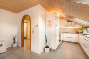 Une cuisine moderne avec des meubles blancs, un plafond en bois et une plante en pot.