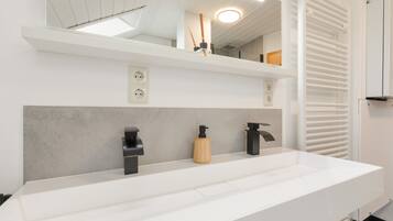 Une salle de bain moderne avec un meuble-lavabo blanc, deux robinets noirs, un distributeur de savon en bois et un miroir au-dessus du lavabo.