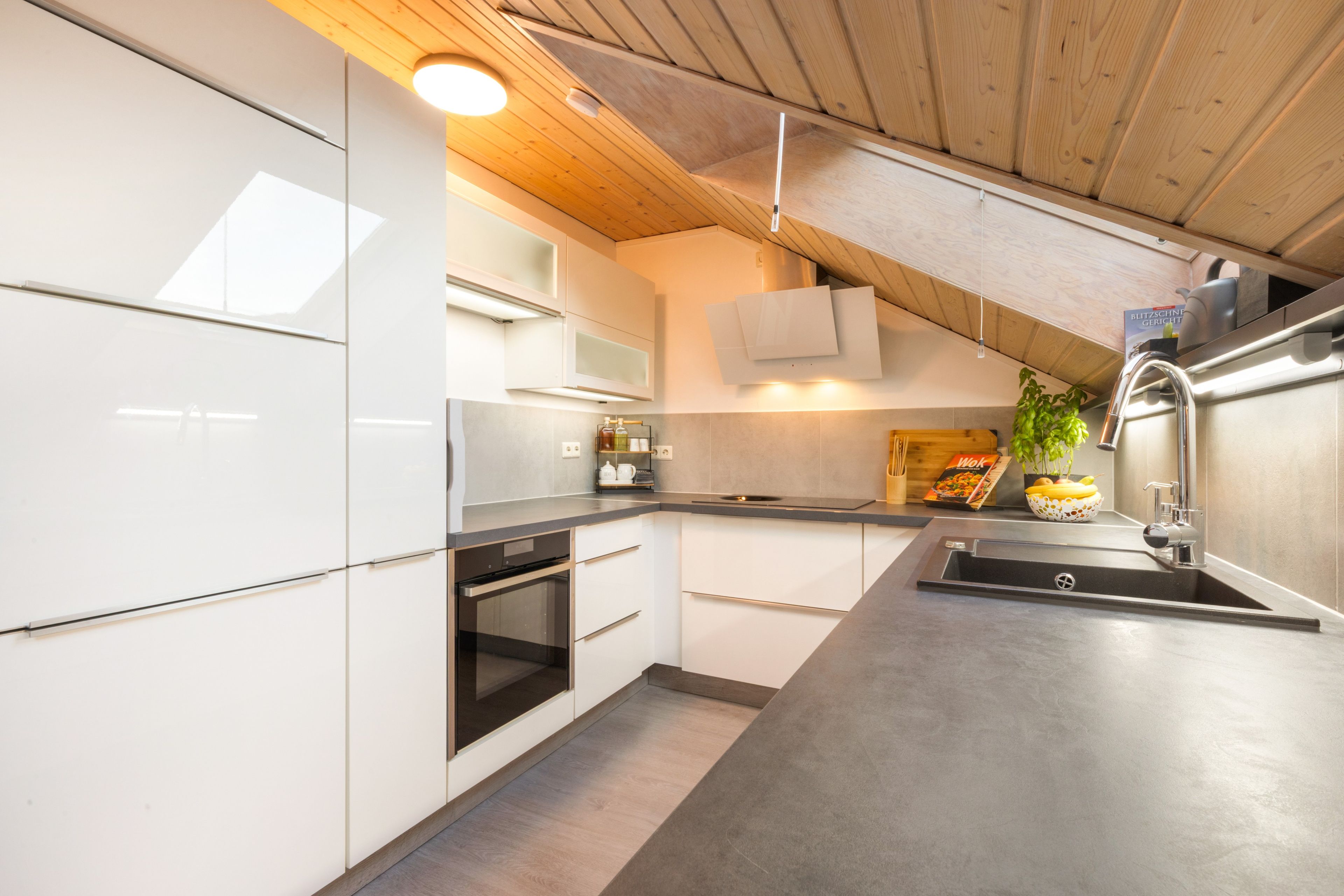 Una cocina moderna con armarios blancos, horno integrado y pileta de acero inoxidable.