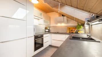 Una cocina moderna con armarios blancos, horno integrado y pileta de acero inoxidable.