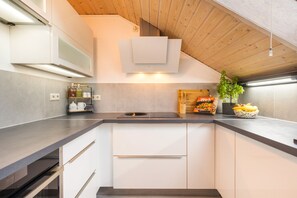 A modern kitchen with a built-in oven, a wooden ceiling, and a countertop with a bowl of fruit and a cookbook.