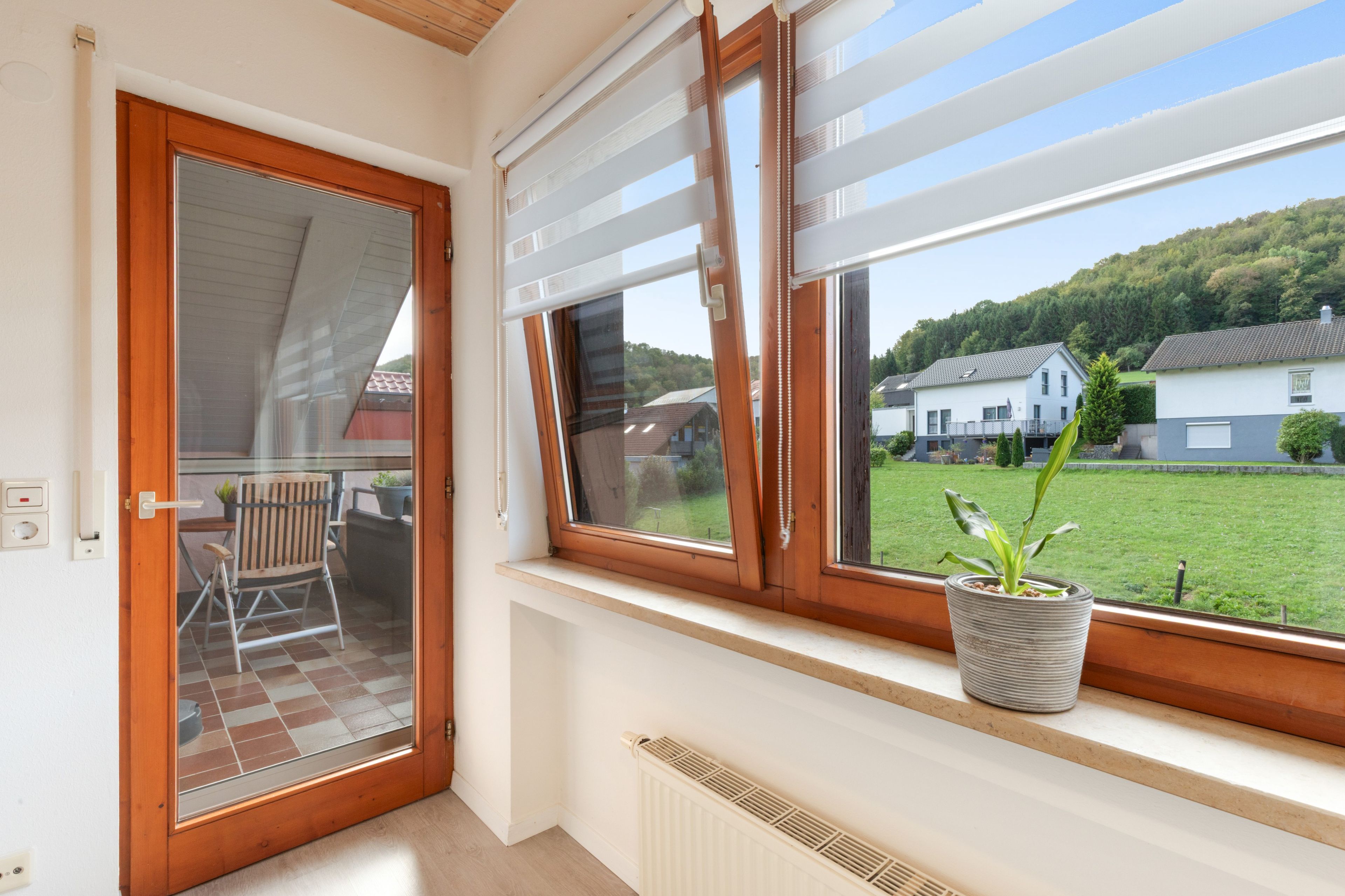 Ein Zimmer mit einer Schiebetür zu einem Außenbereich, einem Fenster mit Blick auf Häuser und einem Heizkörper an der Wand.
