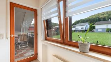Ein Zimmer mit einer Schiebetür zu einem Außenbereich, einem Fenster mit Blick auf Häuser und einem Heizkörper an der Wand.