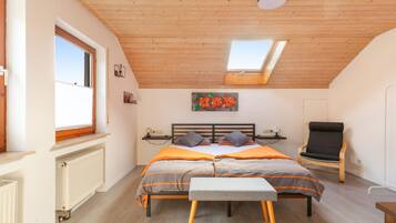Une chambre avec un plafond en pente, un puits de lumière, un lit avec une tête de lit, une table de chevet, une chaise et un radiateur.