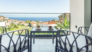 Un balcón con mesa y sillas, con vistas a un pueblo costero con casas y al mar.