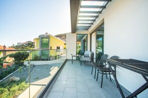A balcony with a glass railing, outdoor furniture, and a view of the surrounding buildings.