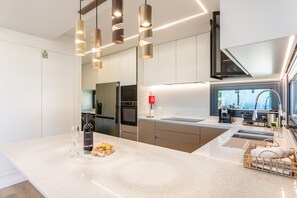 A modern kitchen with stainless steel appliances, a large island with a wine bottle and glass, and pendant lighting.