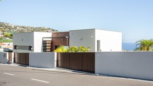Un edificio moderno de dos pisos con techo plano, entrada protegida por una reja y vista al mar.