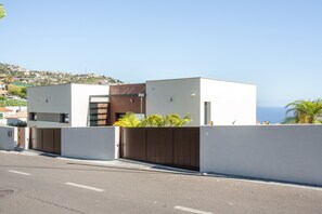 A modern two-story building with a flat roof, a gated entrance, and a view of the sea.