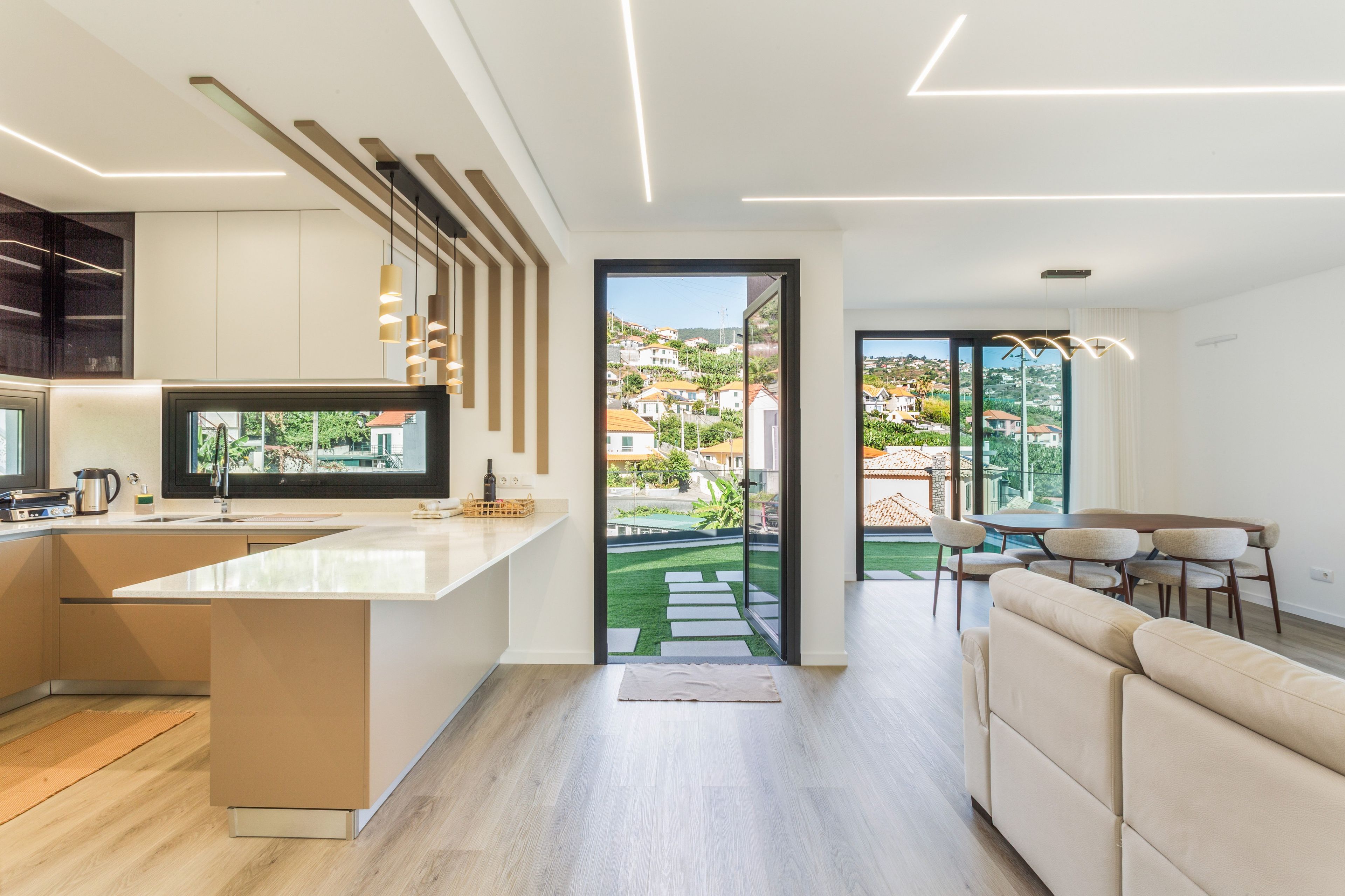 A modern kitchen with a large island, a dining area with a sofa and chairs, and a view of a residential area through a glass door.