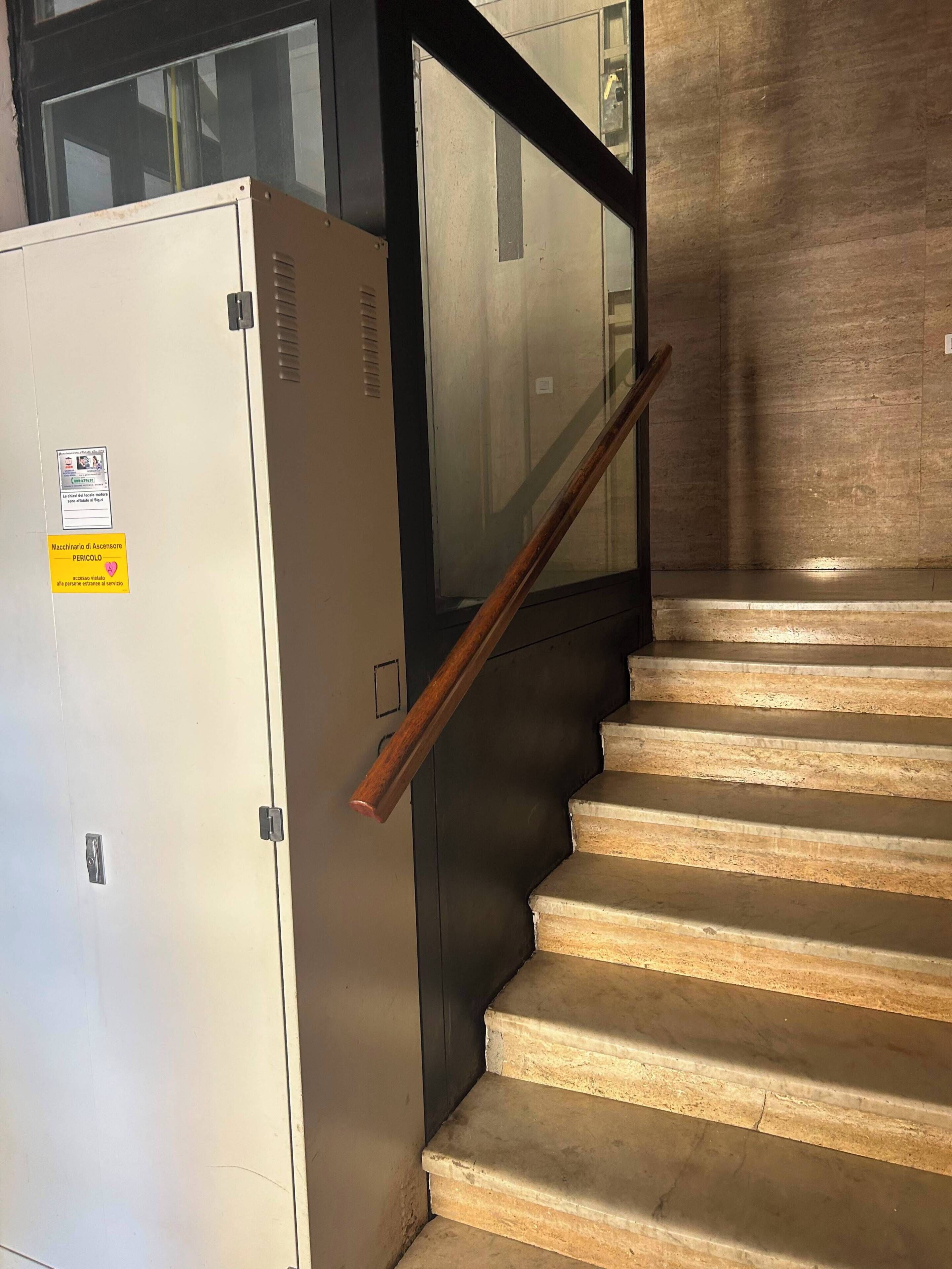 A staircase with a handrail leading to a landing, next to a white cabinet with a yellow sticker.