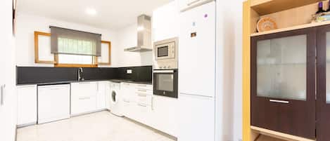 Una cocina moderna con armarios blancos, horno empotrado, microondas y lavavajillas.