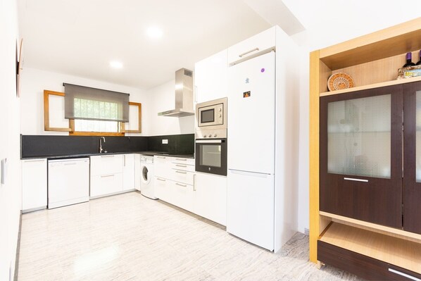 Una cocina moderna con armarios blancos, horno empotrado, microondas y lavavajillas.