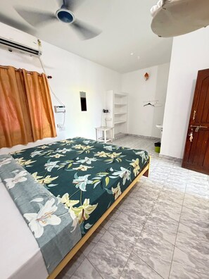 A bedroom with a bed, a ceiling fan, a wardrobe, and a small table.