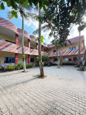 A courtyard with a tiled floor, surrounded by buildings with red and white patterned roofs, and palm trees.