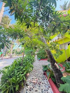 A pathway lined with greenery and a tiled walkway leading to a building with a bright yellow facade.