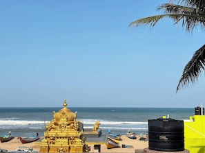 A beach with a golden temple structure, a black water tank, and a clear blue sky.