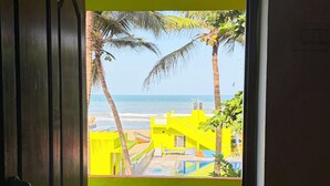 Una puerta que da a un balcón con vista a una playa y palmeras.