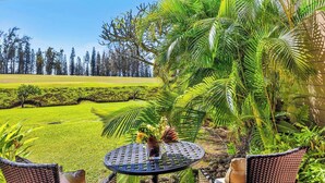 Un patio con una mesa redonda, sillas y vistas a un césped cuidado y árboles.