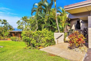 A residential property with a well-maintained lawn, a covered outdoor seating area, and a variety of tropical plants. - Kapalua Ridge | 3 Ocean View Villas, Sleeps 16 | Car Incl. w/ 6+ Nights | ML-4256 by KBM (Lahaina)