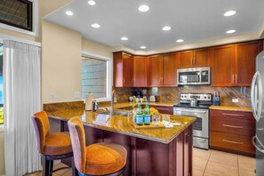 A modern kitchen with wooden cabinets, stainless steel appliances, and a granite countertop. - Kapalua Ridge | 3 Ocean View Villas, Sleeps 16 | Car Incl. w/ 6+ Nights | ML-4256 by KBM (Lahaina)