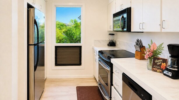 Cocina compacta con refrigerador, microondas, estufa, horno y lavavajillas. Una ventana ofrece vista a zonas verdes.