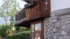 Ein Holzbalkon mit aufwendigen Schnitzereien, eine Steinsäule und eine Treppe zum Eingang.