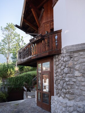 A wooden balcony with intricate carvings, a stone wall, and a staircase leading to the entrance. - Casa di Gio, close to the center with balcony and beautiful views (Cortina d´Ampezzo)