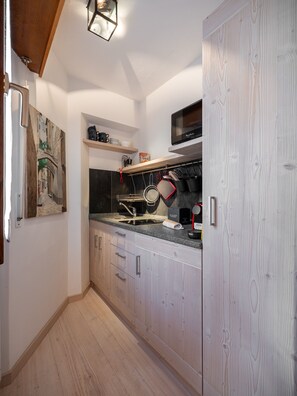 A compact kitchen with wooden cabinets, a microwave, and a hanging pot rack. - Casa di Gio, close to the center with balcony and beautiful views (Cortina d´Ampezzo)