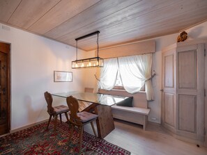 Een eetruimte met een glazen tafel, houten stoelen, een hanglamp, een bank, een raam met gordijnen en een deur.