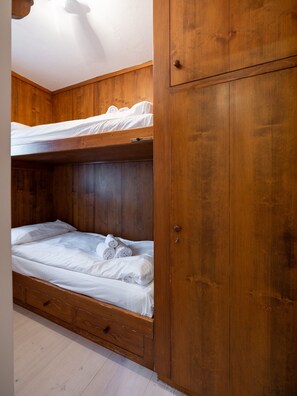 Een stapelbed met houten hoofdbord en lades, een houten garderobe, en een wit plafond.