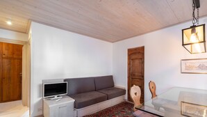 Ein Wohnzimmer mit einer Couch, einem Fernseher, einem Holzschrank, einem Glastisch und einem gemusterten Teppich.