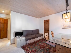 A living room with a sofa, TV, wooden cabinet, glass table, and a patterned rug. - Casa di Gio, close to the center with balcony and beautiful views (Cortina d´Ampezzo)