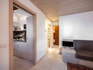 A modern living room with a sofa, a television, and a kitchen area visible through an open door. - Casa di Gio, close to the center with balcony and beautiful views (Cortina d´Ampezzo)