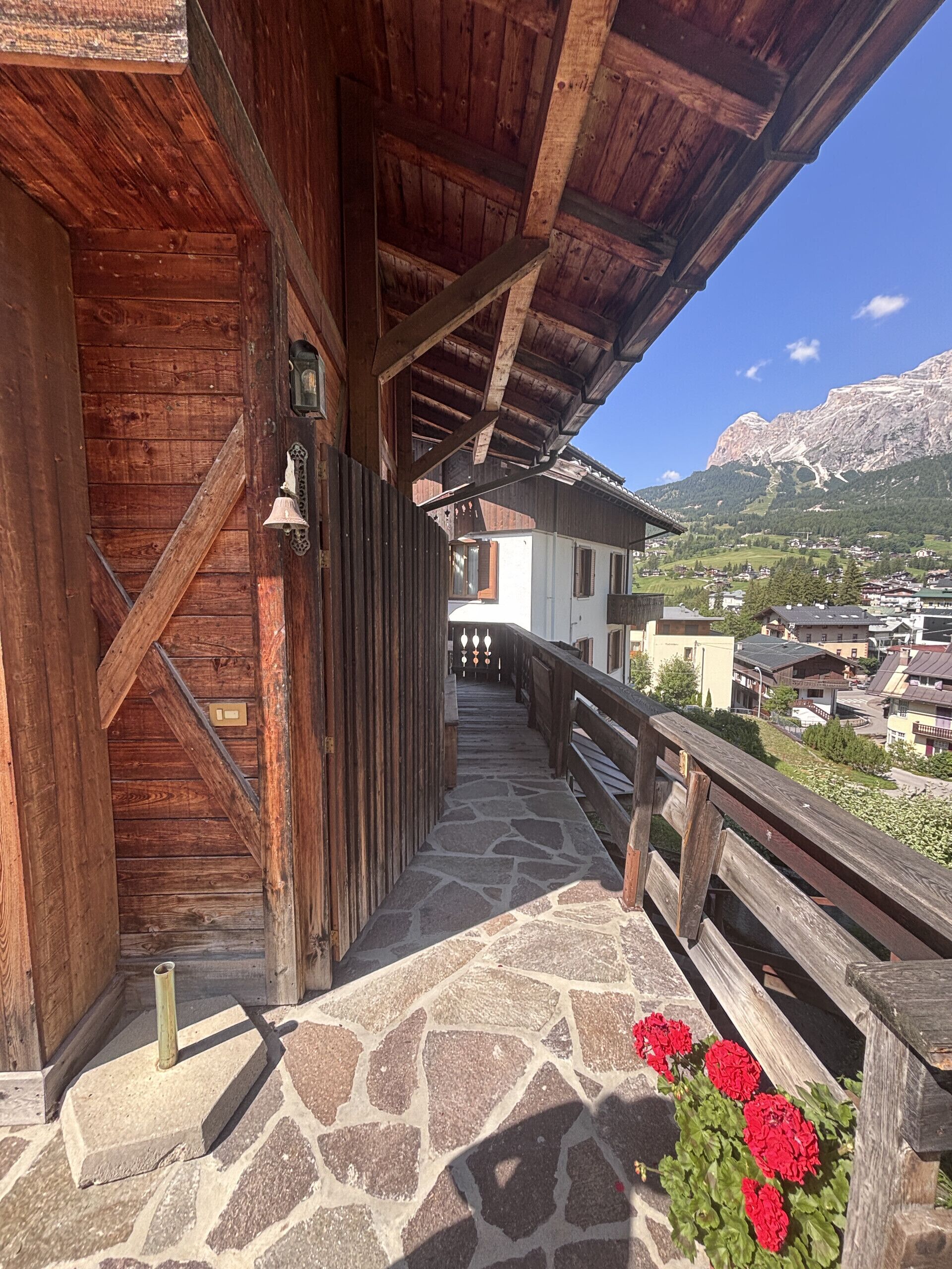 A wooden building with a stone staircase leading to a balcony overlooking a mountainous landscape.