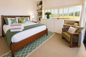 A bedroom with a bed, a chair, a window, and a shelf with plants. - Kapalua Ridge | 2 Ocean View Villas, Sleeps 8 | Car Incl. w/ 6+ Nights | ML-4259 by KBM (Lahaina)