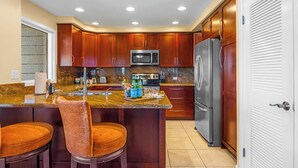 A kitchen with wooden cabinets, a stainless steel refrigerator, a microwave, and a granite countertop. - Kapalua Ridge | 2 Ocean View Villas, Sleeps 8 | Car Incl. w/ 6+ Nights | ML-4259 by KBM (Lahaina)