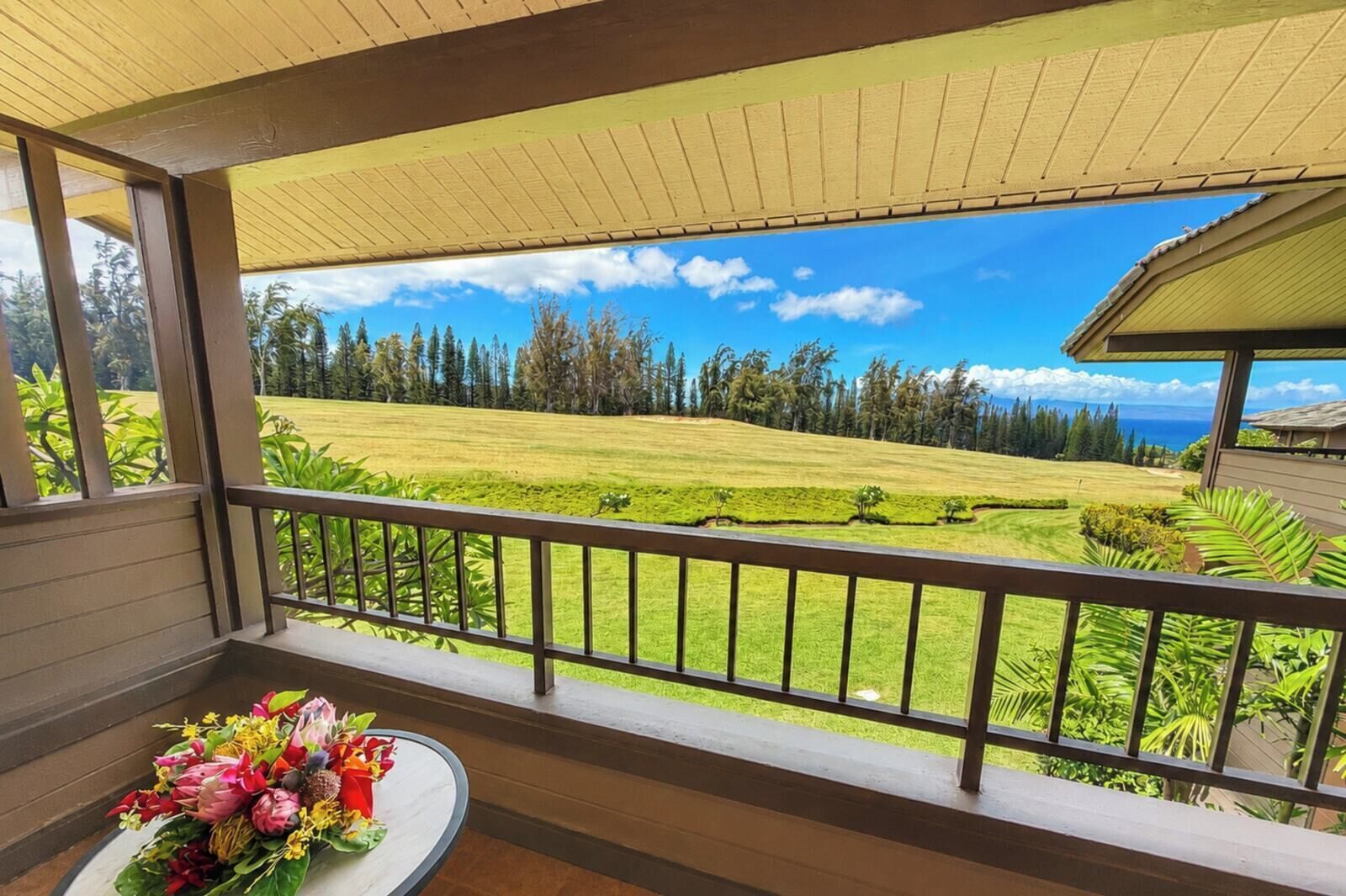 A balcony with a view of a golf course, a table with a floral arrangement, and a covered area with a roof.