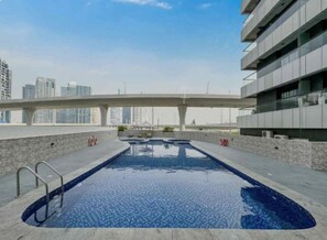 A rooftop swimming pool with a cityscape view, a covered walkway, and a modern building facade. - Partial marina view prime location (Dubai)