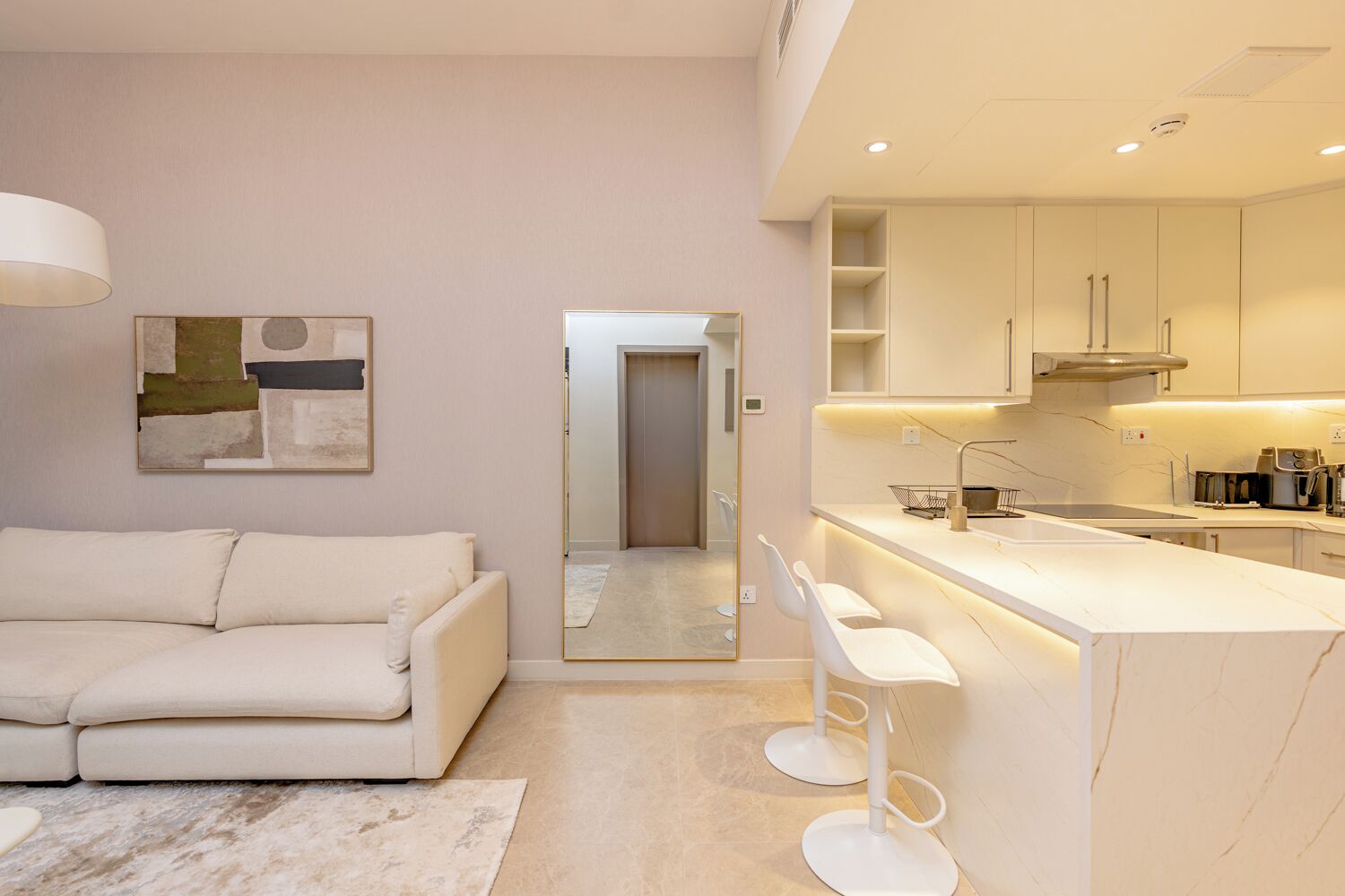 Un interno moderno con un divano bianco, una cucina con mobili bianchi e un grande specchio che riflette l'ambiente.