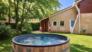 A wooden hot tub in a backyard with a brick house and a tree. - Stunning home in Vlagtwedde with sauna (Vlagtwedde)
