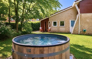 Ein hölzernes Whirlpool im Garten mit einem Ziegelhaus und einem Baum.