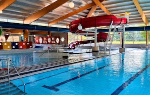 Ein hallenbad mit mehreren Bahnen, einer roten Wasserrutsche und einem Rettungsschwimmerstand.