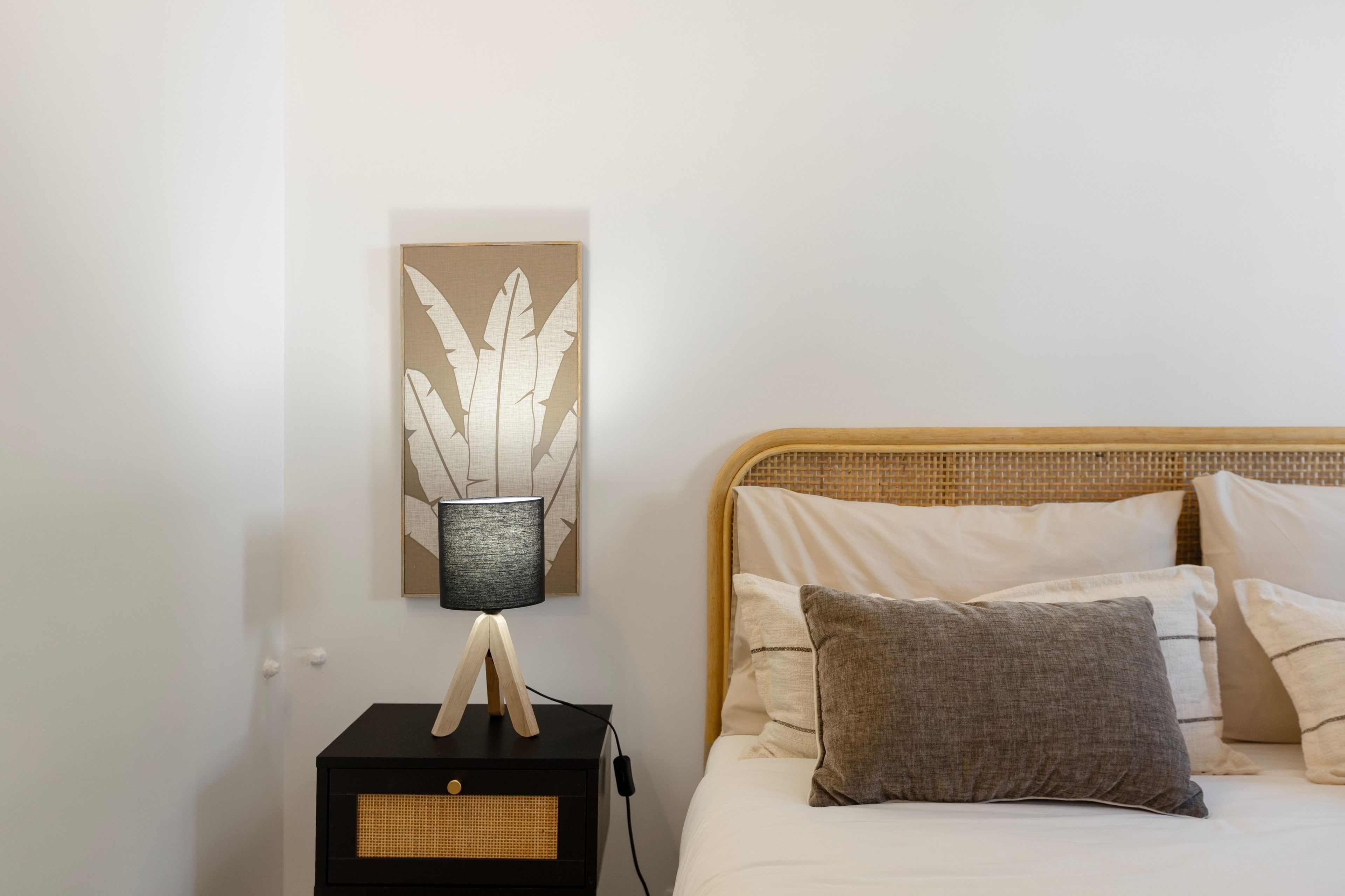 Una camera da letto con un letto, cuscini, un comodino, una lampada e un quadro appeso al muro.
