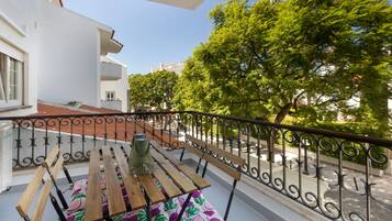 A balcony with a wooden table and chairs, a metal railing, and a view of trees and buildings.