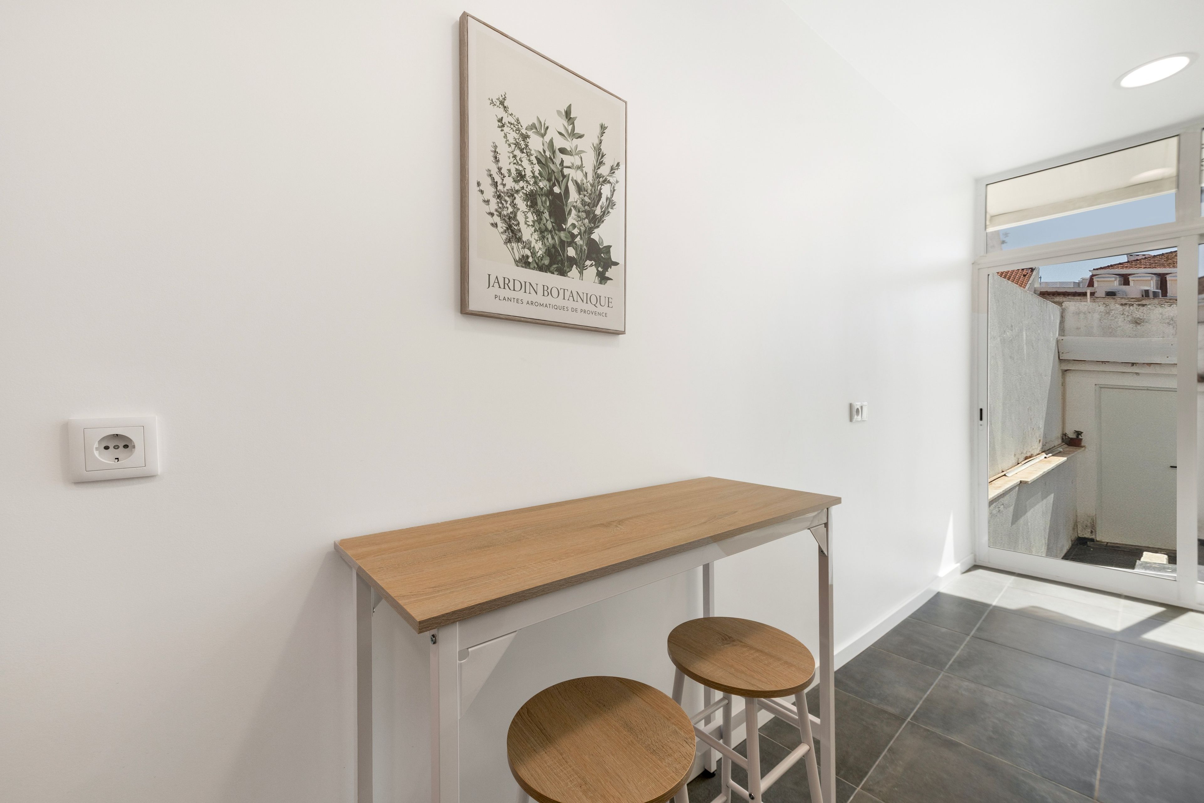 A hallway with a white wall, a framed botanical print, a wooden console table, and two stools.