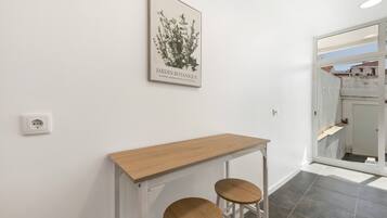 A hallway with a white wall, a framed botanical print, a wooden console table, and two stools.